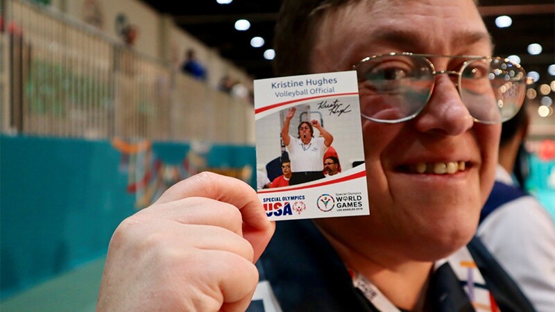 Kristine poses with her Special Olympics USA World Games trading card and smiles.