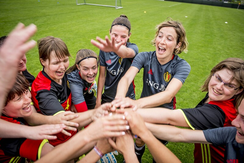 European Football female group on the field standing in circle with all of their hands in the the middle one on top of another in celebration.