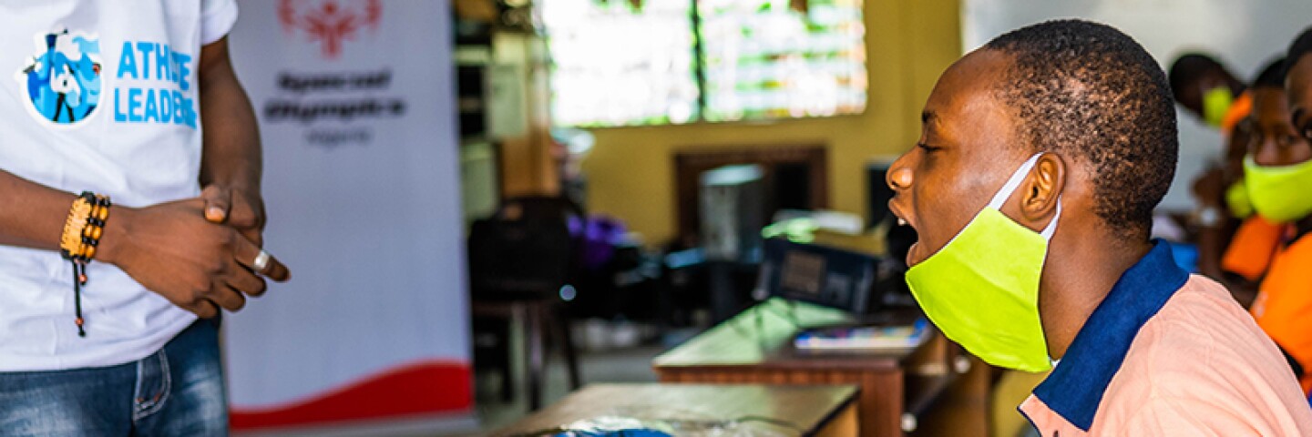A young man sitting at a desk and asking the class leader a question.