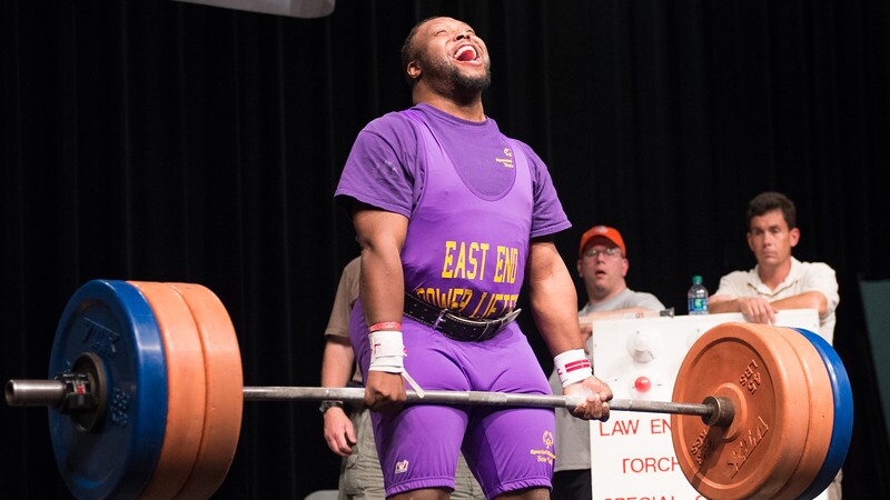 Young adult male athlete performing deadlift as judges and officials watch.