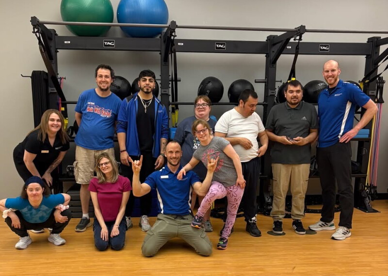 A group of people stand in front of fitness equipment and smile for a photo.