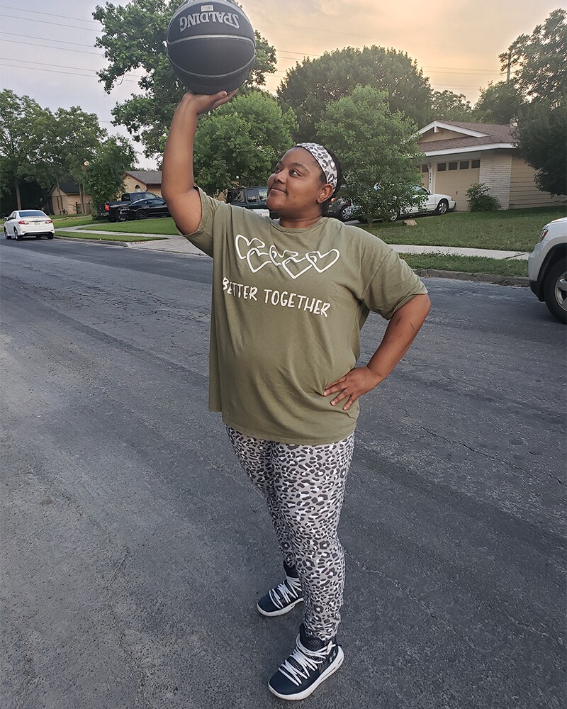 Tiffany Renee Evans in a green Better Together t-shirt standing outside posing with a basketball.