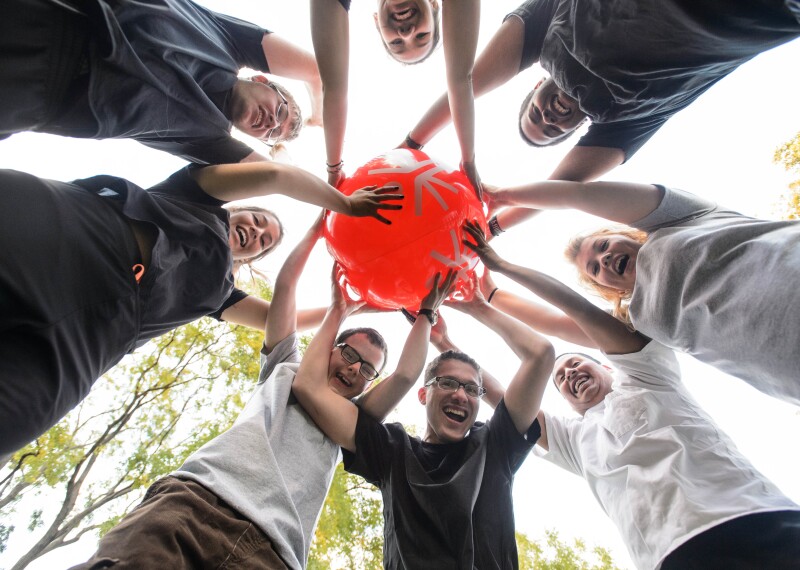 8 students standing in a circle hold up a red play unified beach ball 