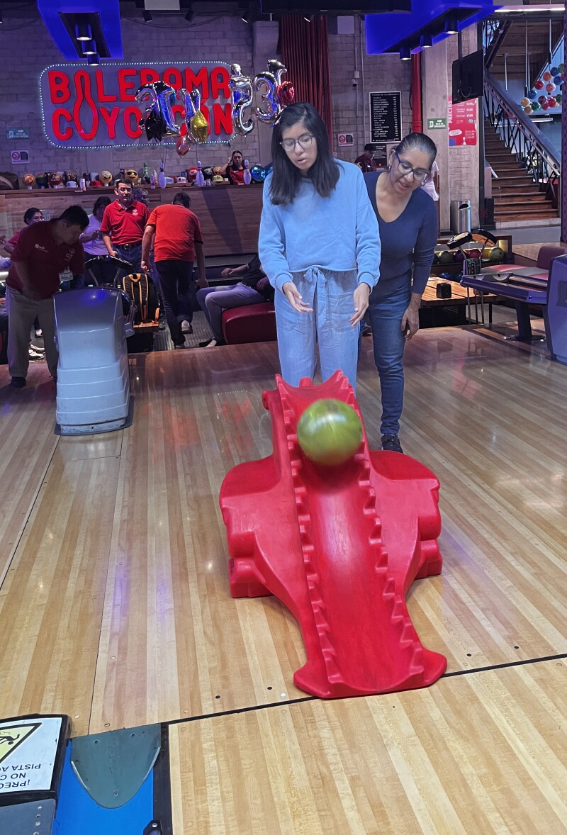 Dois homens estão no início de uma pista de boliche e empurram uma bola de boliche por uma rampa.