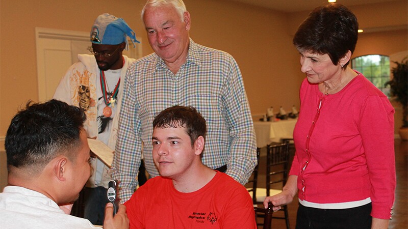 Ann Costello and Tom Golisano watch an athlete receive an eye exam.