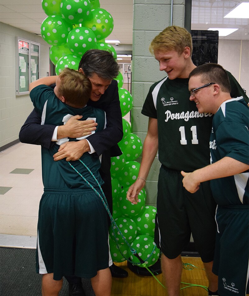 Tim Shriver Hugging and athlete; two other spectators look on.
