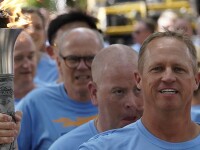A man in a Final Leg blue t-shirt holds a lit torch with several other men lined up behind him.