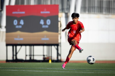 Una mujer con equipación/uniforme rojo patea un balón en un campo de fútbol.