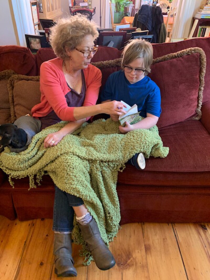 Kari and Thorin filming at their home in Portland, Maine. Kari and Thorin sitting on a couch with a green blanked covering their legs while Thorin reads a book as Keri flips the pages.