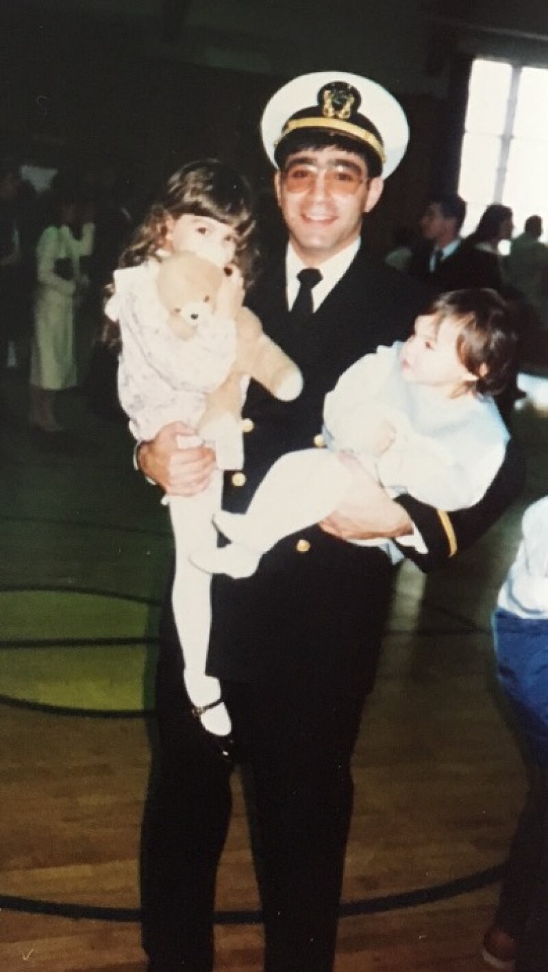 A man wearing a military uniform holds two small children.