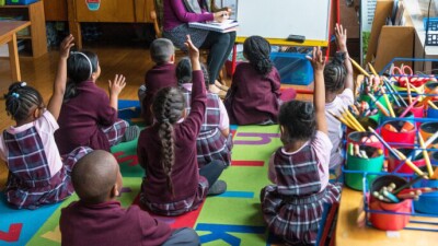 Kids in a class room raising their hands.