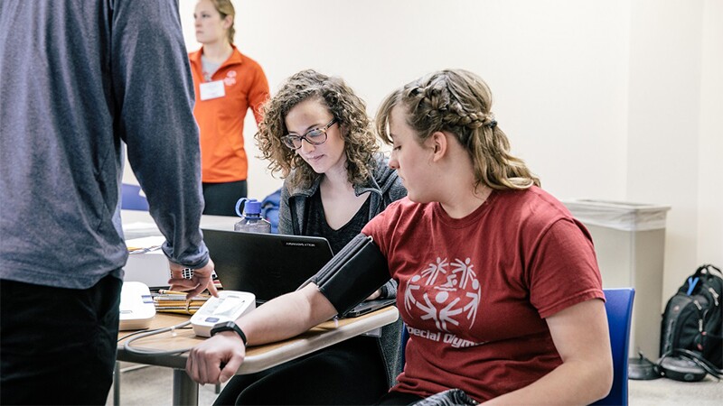 Athlete receiving a blood pressure test while two others stand/sit beside her.