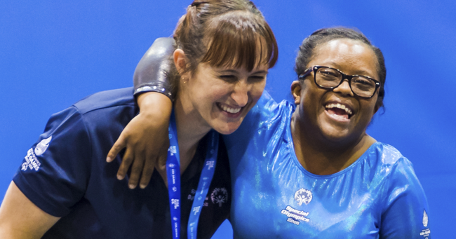 A smiling Special Olympics gymnast wraps her arm around her coach as they celebrate her performance at the 2018 Special Olympics USA Games