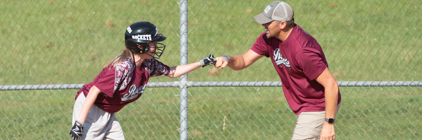 Female baseball player fist-bumping a coach.