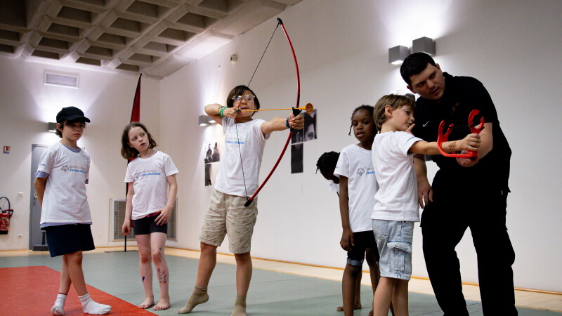 athlete aiming a bow and arrow, another athlete is being assisted in aiming