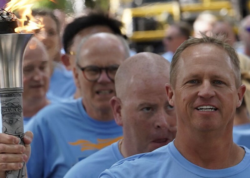 A man in a Final Leg blue t-shirt holds a lit torch with several other men lined up behind him.