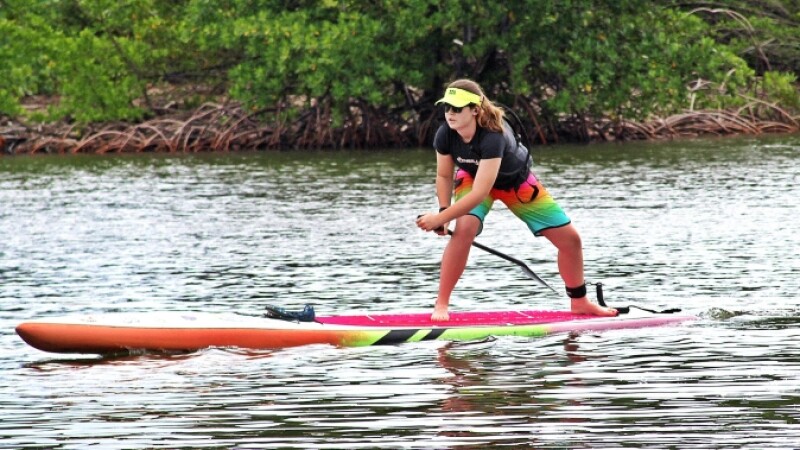 Special Olympics athlete stand up paddleboards down waterway. 