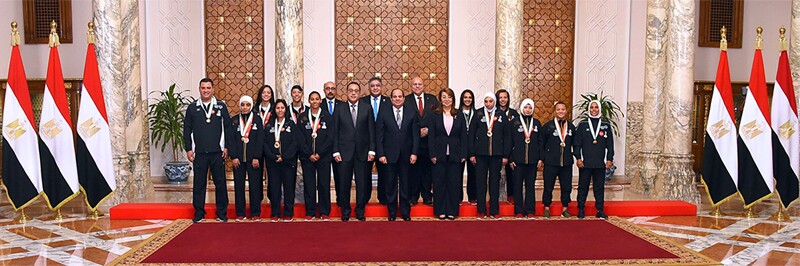 The Egyptian Unified Football team and the president of Egypt lined up in front of a wall with 3 Egyptian flags on each side.