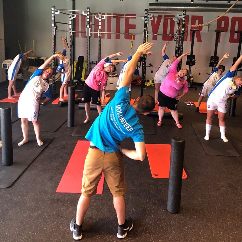 Athletes working out and following the instructions of a volunteer instructor while stretching out in a gym.