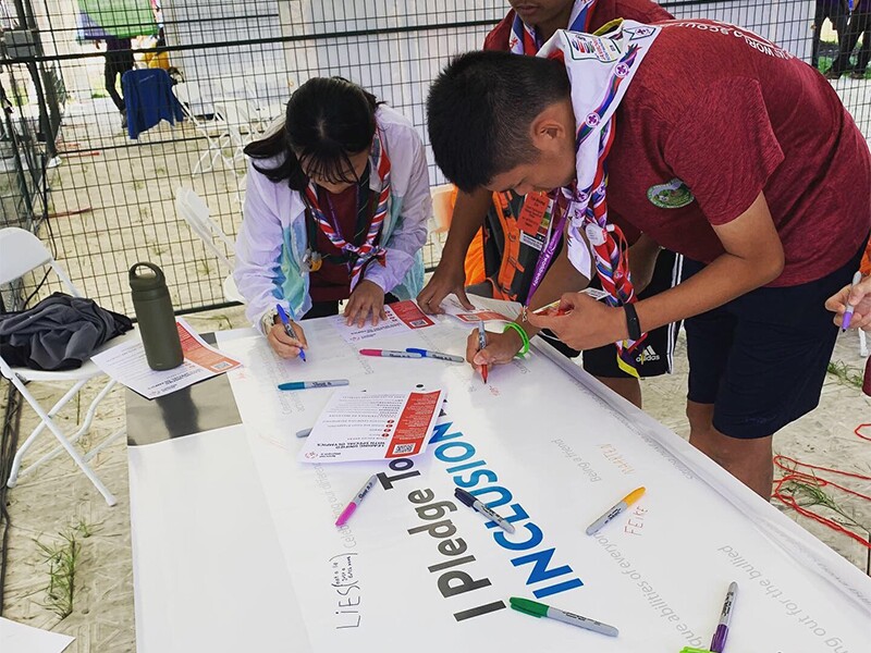 A group of three scouts are standing at a table signing the Inclusion Pledge.