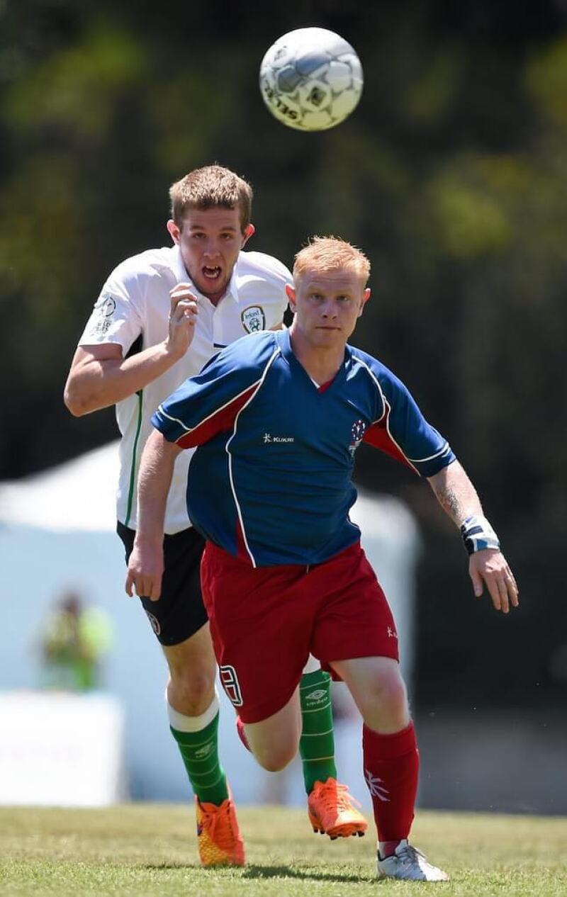 A man runs at the soccer ball. He is wearing a blue and red uniform. A player from a different team runs after the ball behind him.