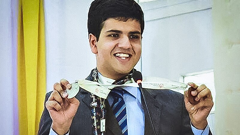 Haseeb Abbasi on stage standing behind a podium and microphone shows his medals.