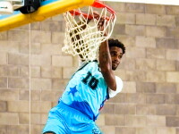 Ryan, a Special Olympics Southern California athlete, hangs from the rim after a powerful dunk as spectators watch from the sideline.