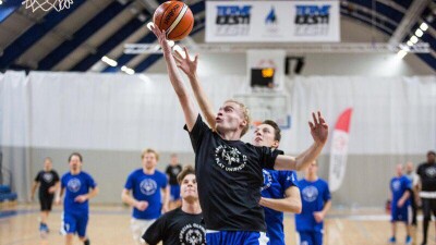 One player jumps for a layup shot; another player attempts to block the shot.