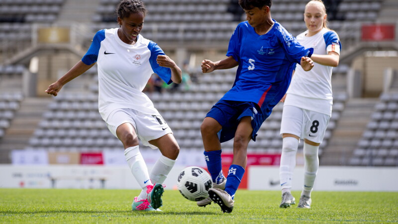 Two footballers from opposing team on the pitch, going for the football. 