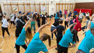Participants in blue t-shirts all lean to their right with their arms overhead stretching.