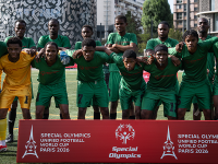 A soccer team poses for a photo. They are wearing green uniforms and standing behind a red sign that says "Special Olympics Unified Football World Cup Paris 2026". 