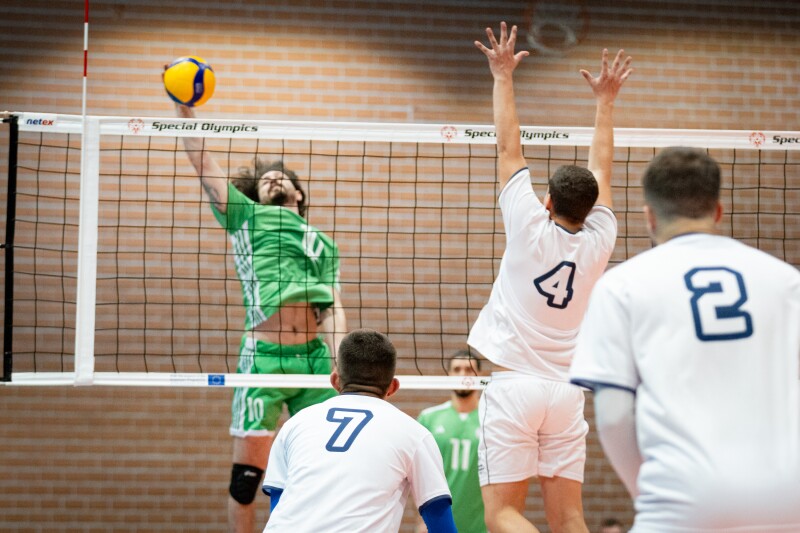 An Iraqi player jumps into the air, spiking the ball as a Serbian player jumps into the air to volley the shot