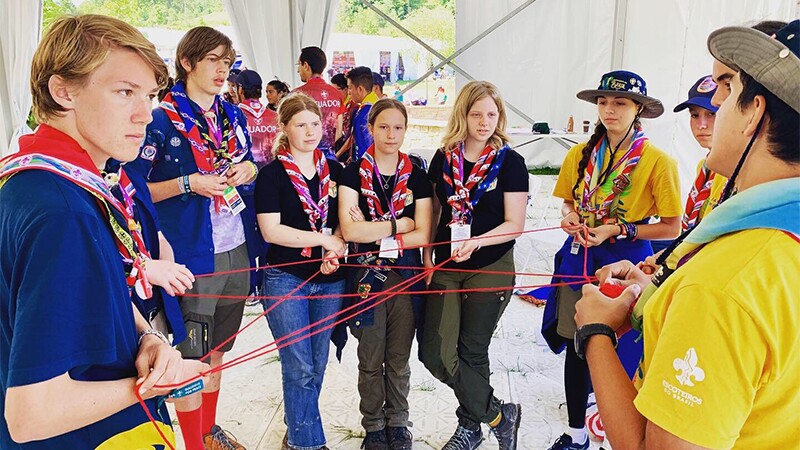 A group of 8 young scouts holding a red string—that each person is holding—to represent inclusion.