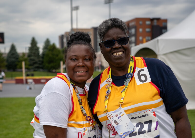 Dos atletas de Olimpiadas Especiales Maryland, vestidos con sus uniformes de equipo, sonríen y se abrazan en un campo de competición cubierto de hierba tras competir en lanzamiento de mini jabalina en los Juegos de Estados Unidos de 2026.