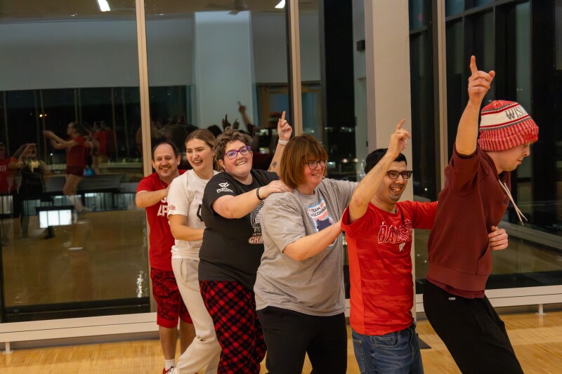 Un grupo de personas forman una fila de conga con las manos sobre los hombros del otro.