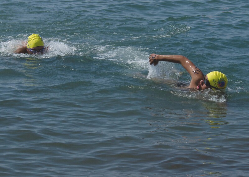 Two athletes with yellow caps swimming in the water.