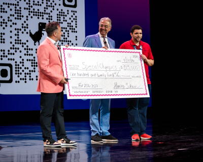 Three people holding a large-sized check while standing on a stage.